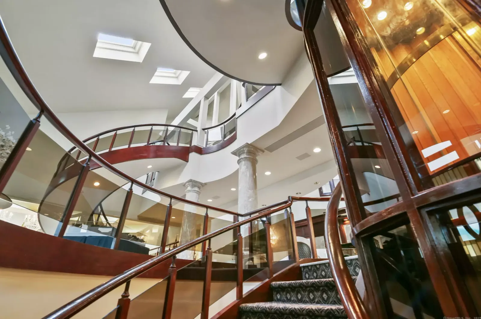 The curved staircase beside the glass elevator.